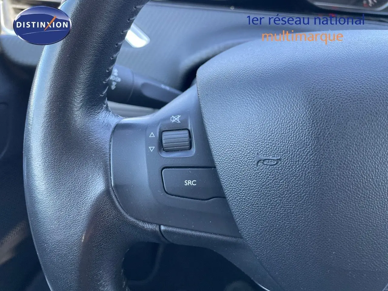Gros plan sur le volant noir du Peugeot 2008 blanc, montrant les commandes audio intégrées à gauche.