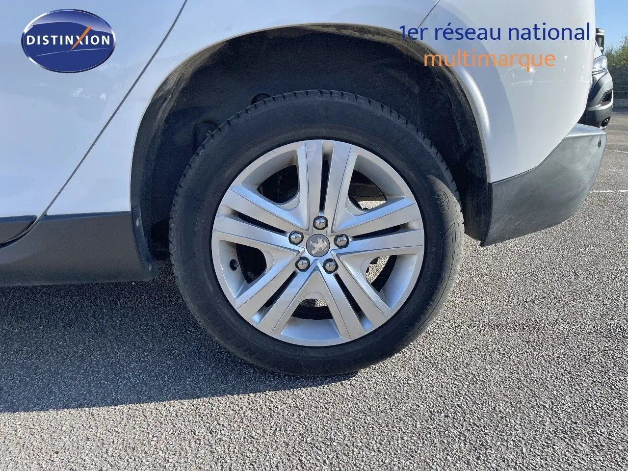 Gros plan sur la roue avant gauche d'un Peugeot 2008 blanc avec jante alliage et logo lion central.