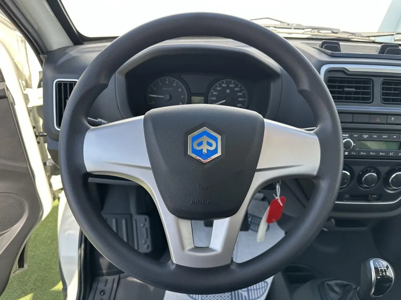 Vue intérieure centrée sur le volant noir et argenté avec logo Piaggio, tableau de bord et levier de vitesses manuelle visibles.