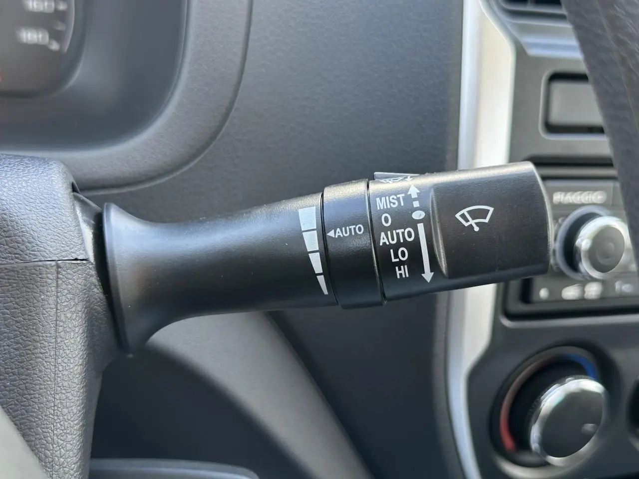 Gros plan sur la commande d'essuie-glace du Piaggio Porter blanc, avec tableau de bord et radio en arrière-plan.