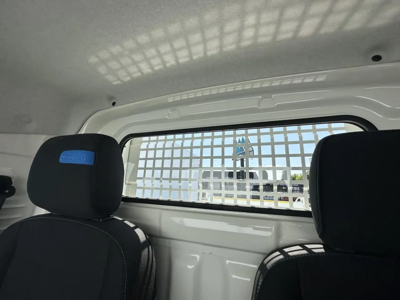 Vue intérieure arrière du Piaggio Porter blanc 2024 avec grille de séparation et sièges noirs marqués Piaggio.