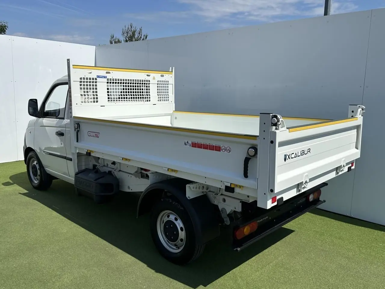 Vue 3/4 arrière droite du Piaggio Porter blanc avec benne longue et ridelle Excalibur sur fond extérieur.