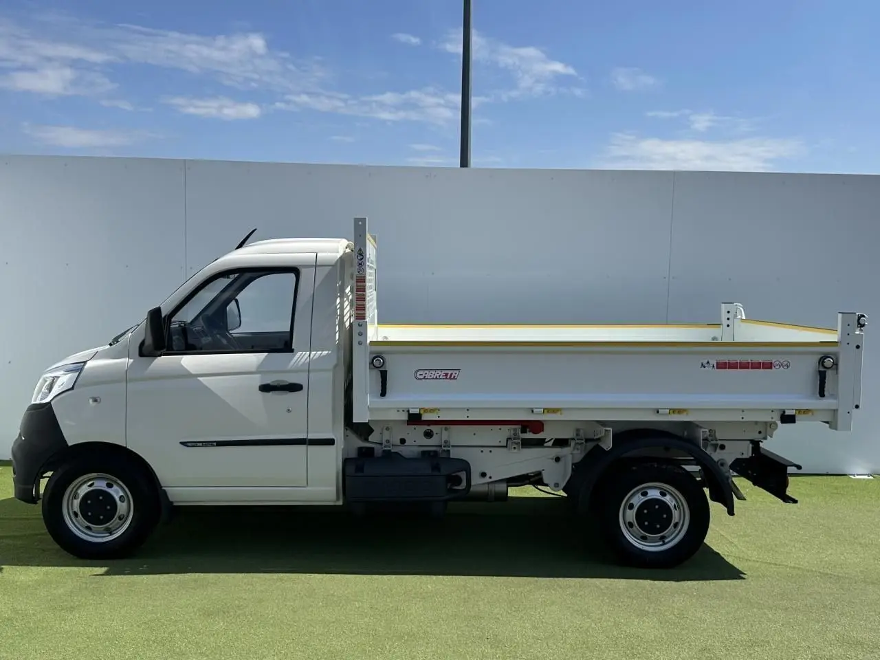Vue de profil côté gauche d'un Piaggio Porter blanc avec benne longue Cabreta sur fond extérieur clair.