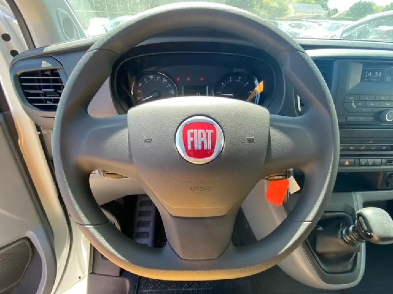 Vue intérieure centrée sur le volant noir avec logo Fiat rouge du FIAT Scudo Fourgon blanc, levier de vitesses manuel visible.