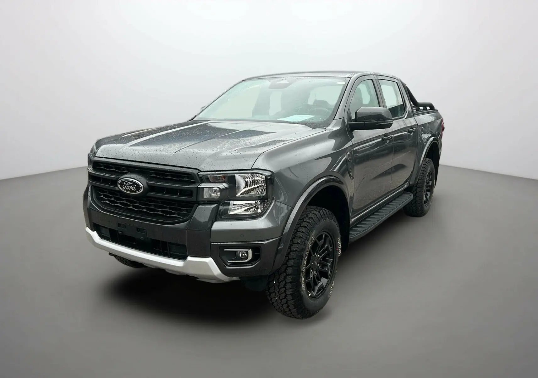 Ford Ranger 2025 gris carbone en 3/4 avant droit, avec calandre noire et roues tout-terrain marquées Tremor Cover.