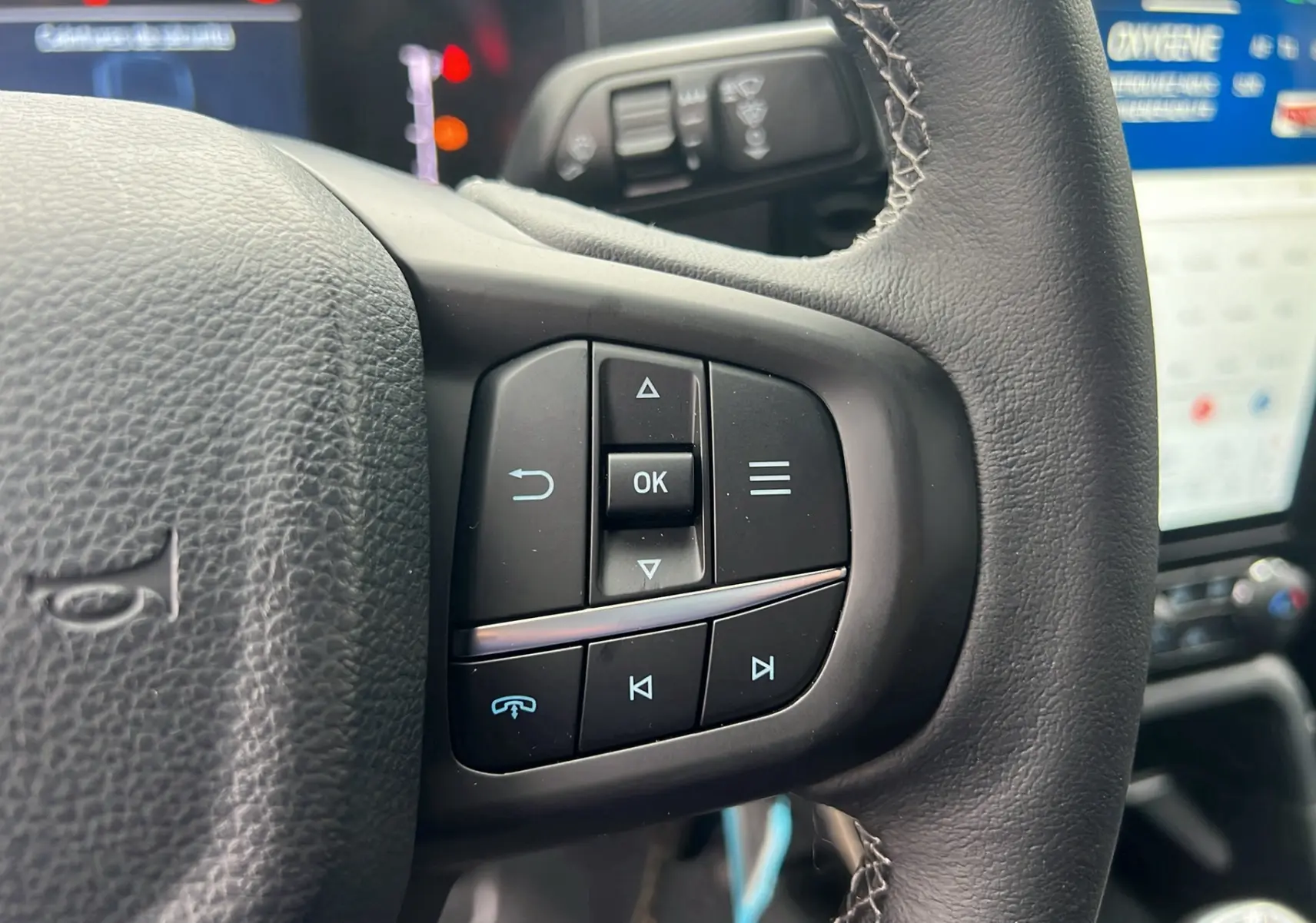 Gros plan sur les commandes au volant du Ford Ranger 2025 gris carbone, avec écran tactile en arrière-plan.