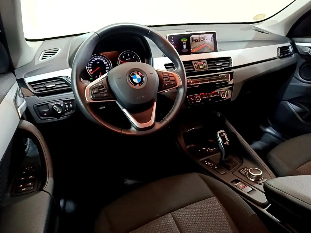 Vue intérieure côté conducteur du BMW X1 noir 2021, avec volant cuir multifonctions et écran central affichant la caméra de recul.