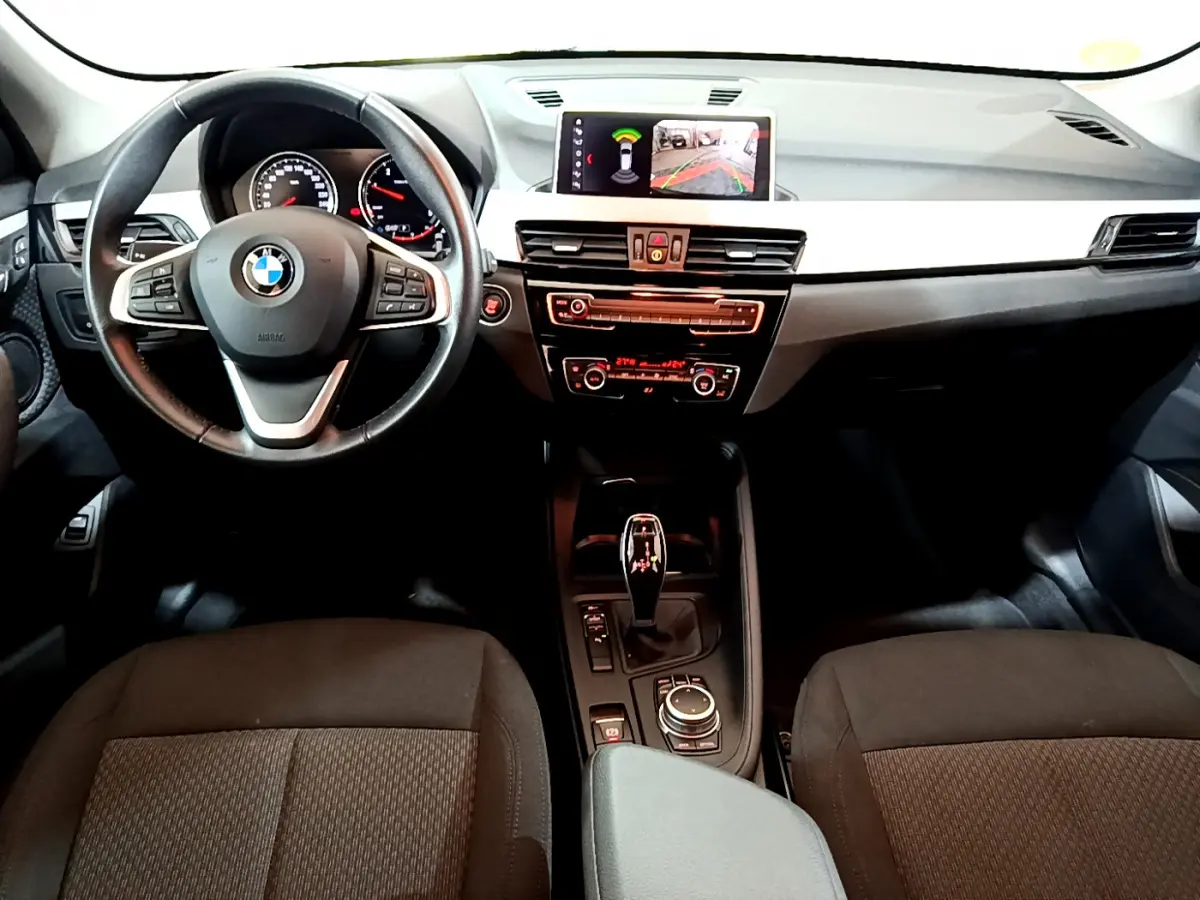 Vue intérieure avant du BMW X1 2021 noir, tableau de bord avec écran central affichant la caméra de recul.