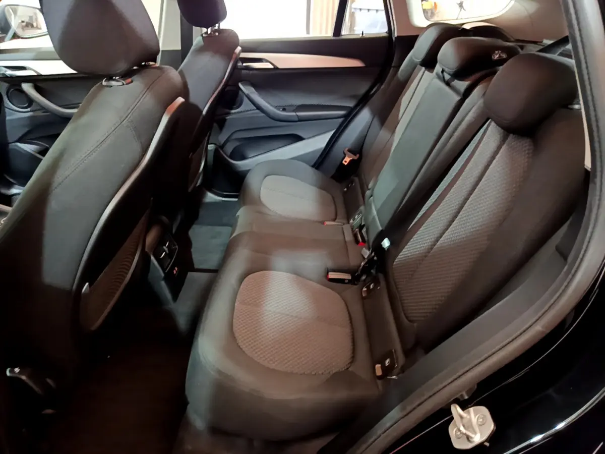 Vue intérieure côté droit des sièges arrière noirs en tissu du BMW X1 sDrive16d Lounge 2021, avec portes ouvertes.