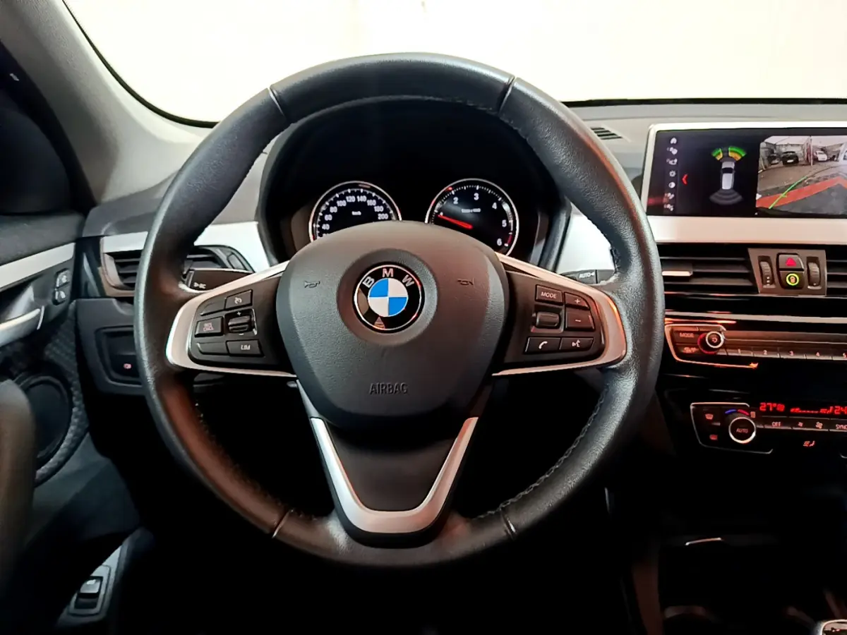 Vue intérieure centrée sur le volant cuir multifonctions d'une BMW X1 2021 avec tableau de bord et écran multimédia.