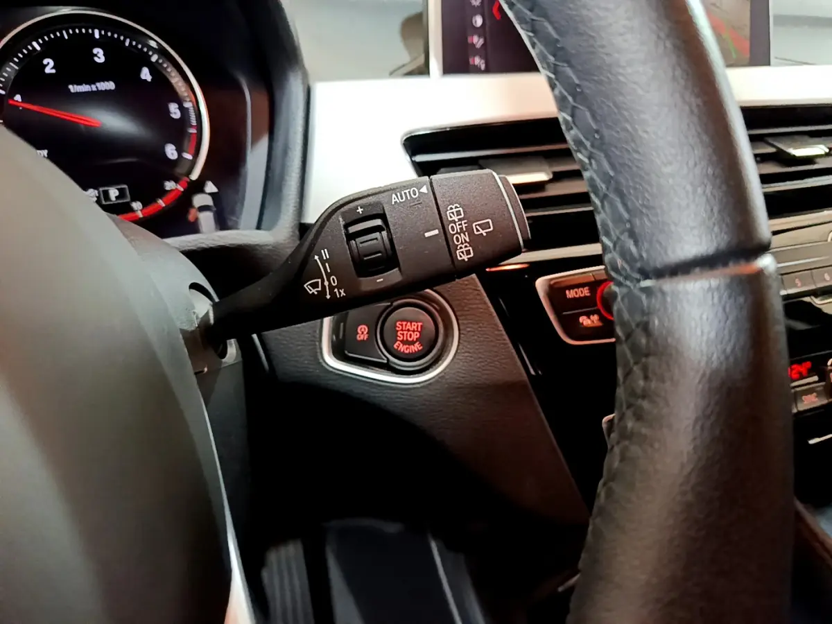 Détail intérieur du BMW X1 2021 noir montrant le commodo d’essuie-glace, bouton start/stop et partie du volant cuir.