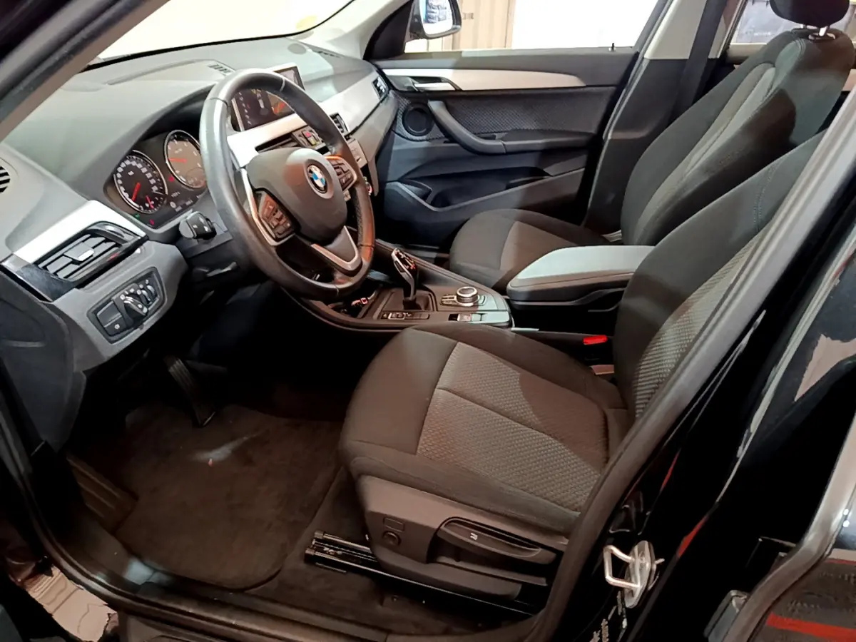 Vue intérieure côté conducteur du BMW X1 noir, montrant le volant cuir multifonctions et la console centrale avec molette.
