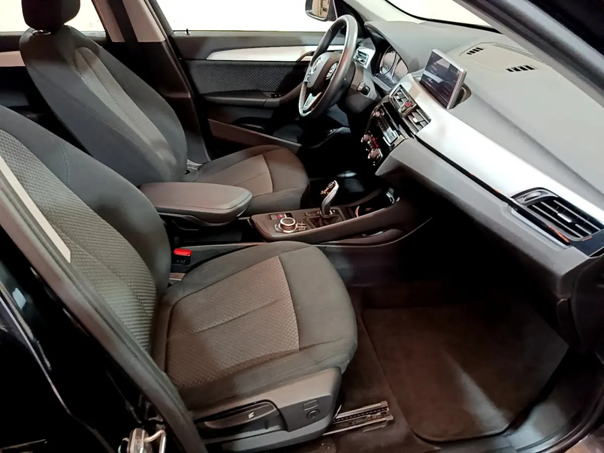 Vue intérieure côté conducteur de la BMW X1 sDrive16d Lounge 2021 avec sièges tissu gris et tableau de bord moderne.