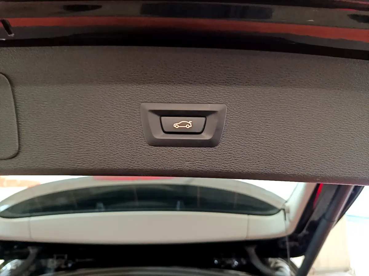 Gros plan sur le bouton d'ouverture électrique du coffre, intérieur du hayon noir du BMW X1 sDrive16d Lounge 2021.