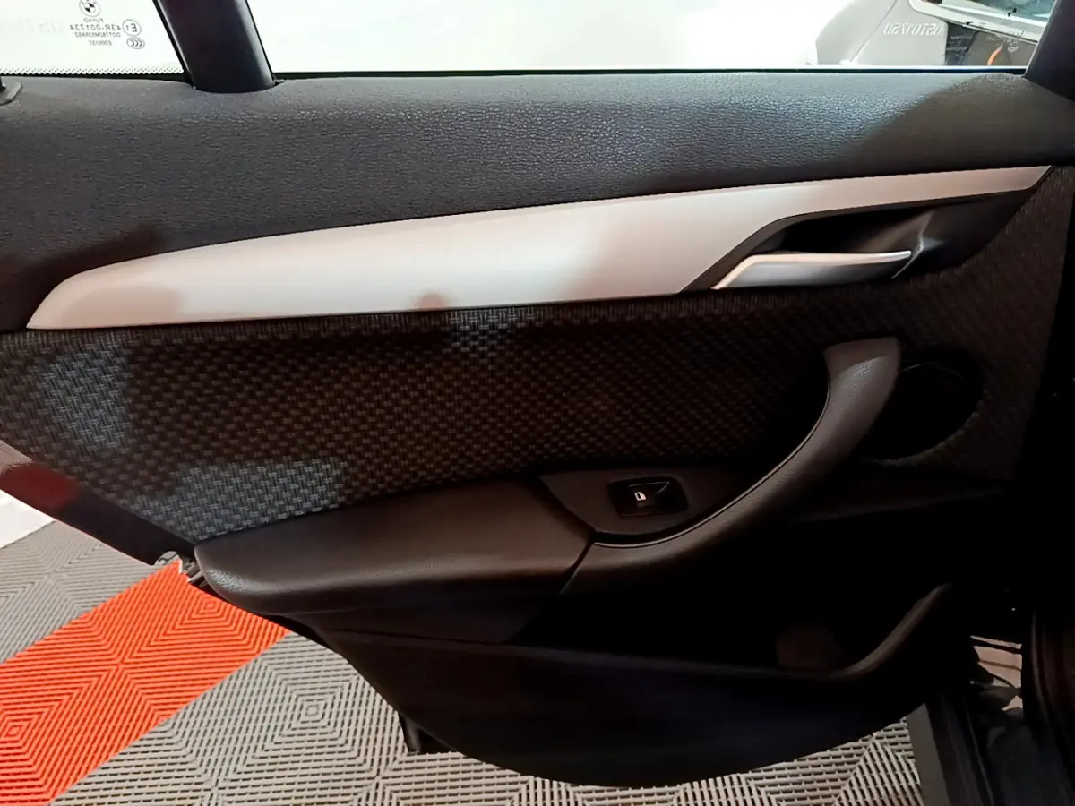 Vue intérieure côté gauche de la porte d’une BMW X1 noire, avec garniture noire texturée et poignée argentée.