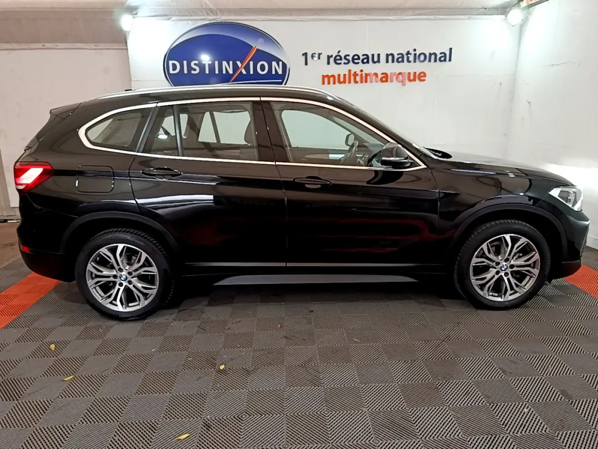 BMW X1 sDrive16d noir vue de profil côté gauche, stationné en intérieur avec jantes alliage visibles.