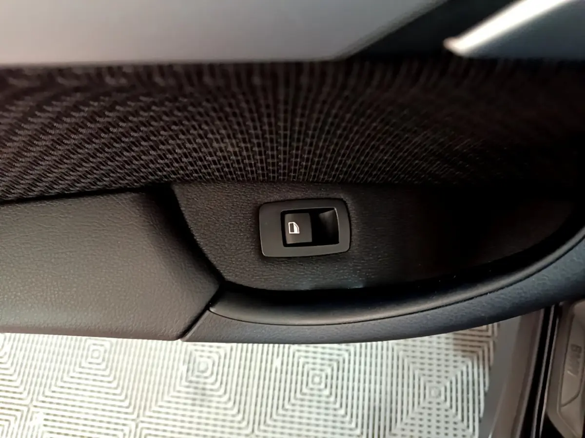 Bouton de verrouillage de porte noir sur panneau intérieur en cuir noir, vue rapprochée côté conducteur d'un BMW X1 noir.