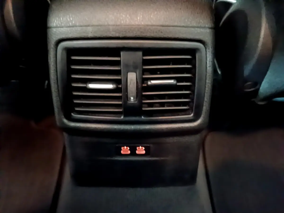 Détail des aérateurs arrière noirs avec commandes de chauffage rouge sur la console centrale d'un BMW X1 noir.