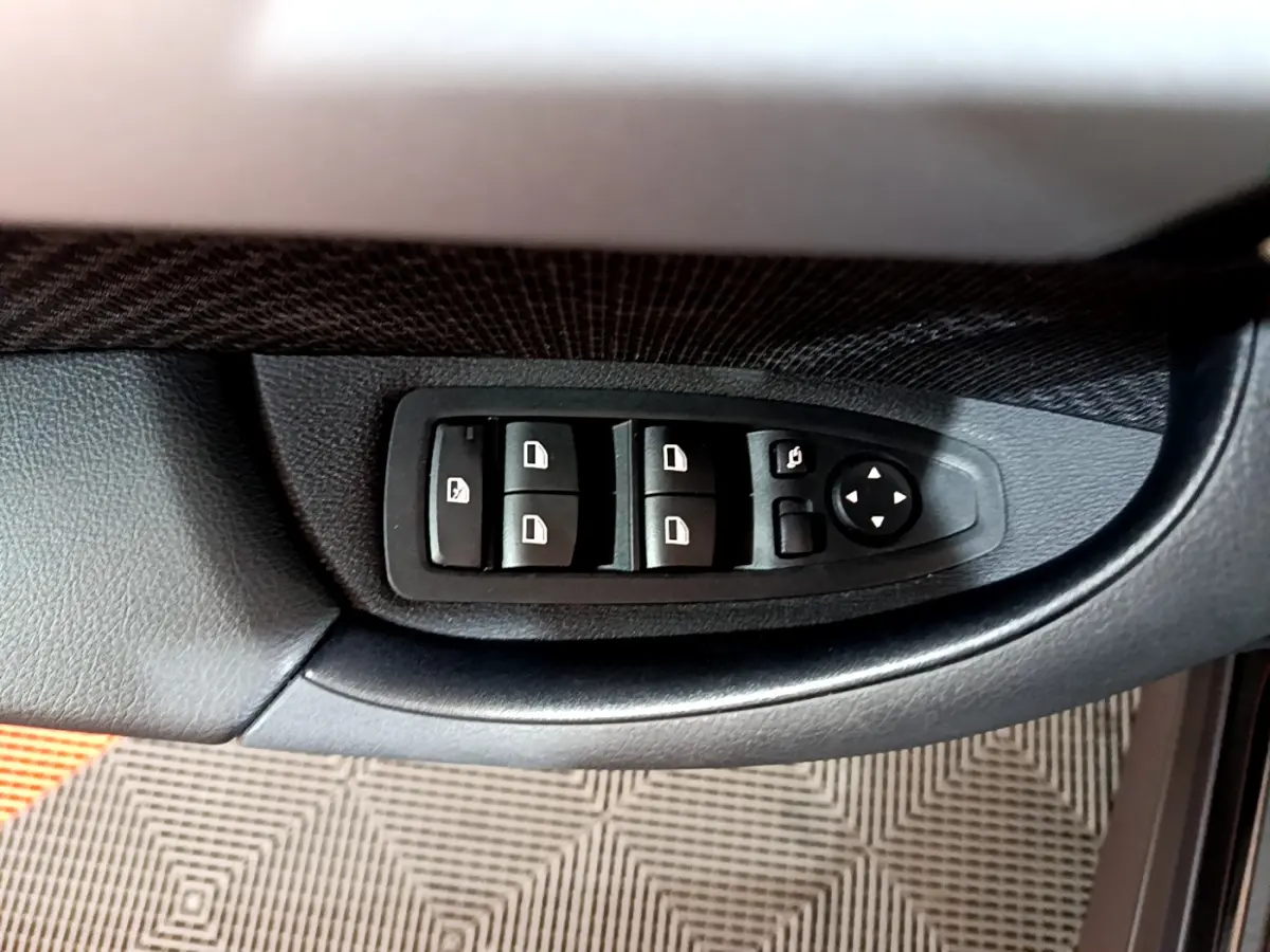 Gros plan sur les commandes de lève-vitres et rétroviseurs côté conducteur d'une BMW X1 noire 2021.