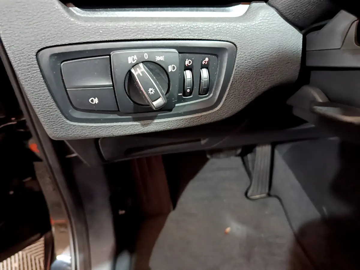 Détail du tableau de bord noir du BMW X1 sDrive16d Lounge 2021, avec commandes d’éclairage et pédale visible.