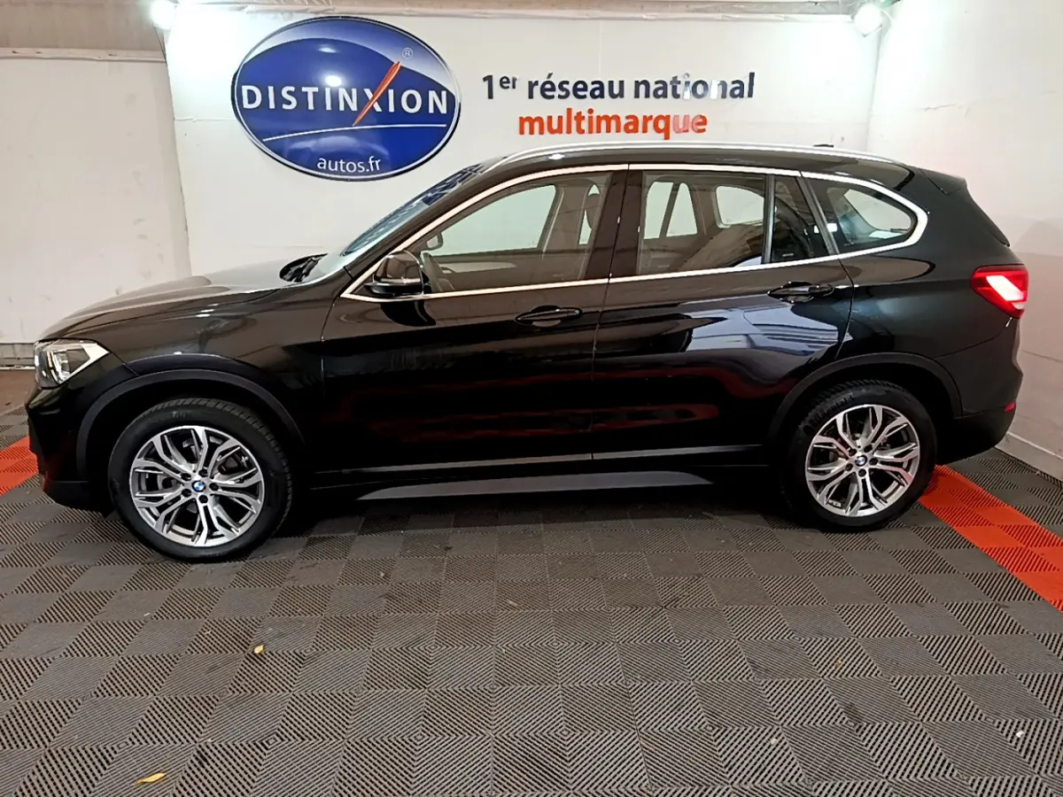 BMW X1 sDrive16d noir vue de profil côté gauche, avec jantes alliage et rétroviseurs électriques dans un showroom.