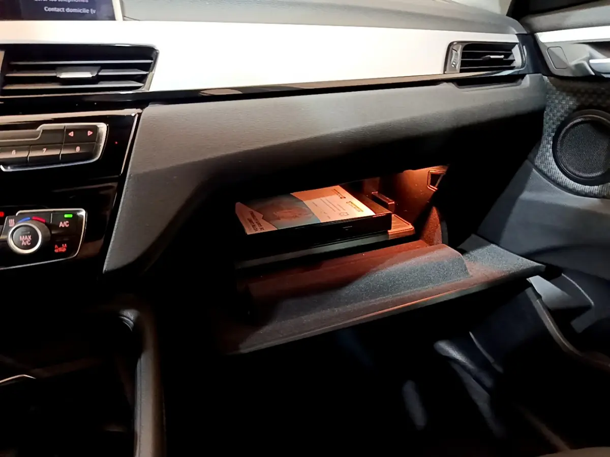 Gros plan sur la boîte à gants ouverte du BMW X1 sDrive16d Lounge 2021, intérieur noir avec éclairage intérieur.