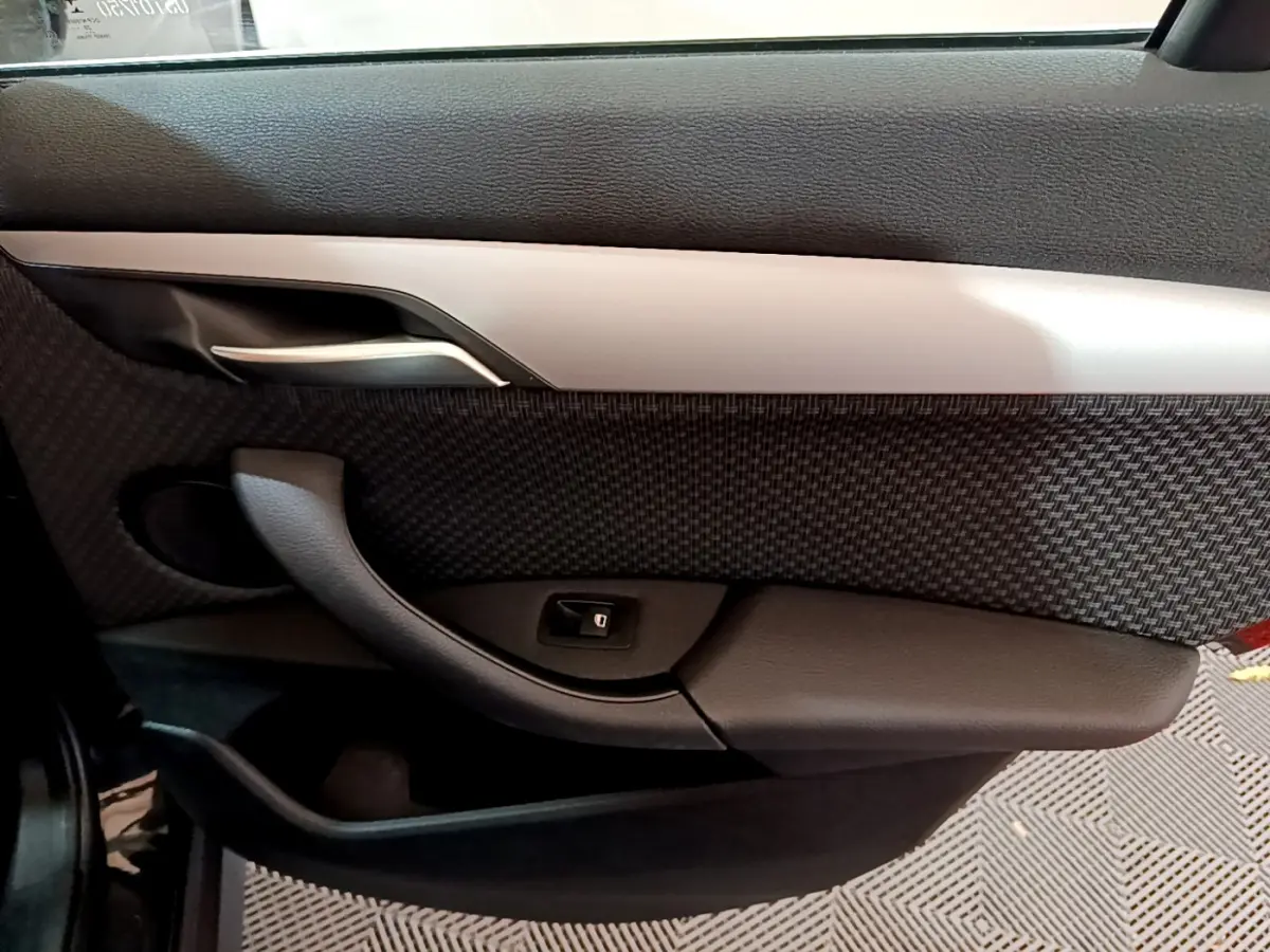 Vue intérieure du panneau de porte côté gauche de la BMW X1 sDrive16d Lounge 2021, avec insert tissu et poignée argentée.