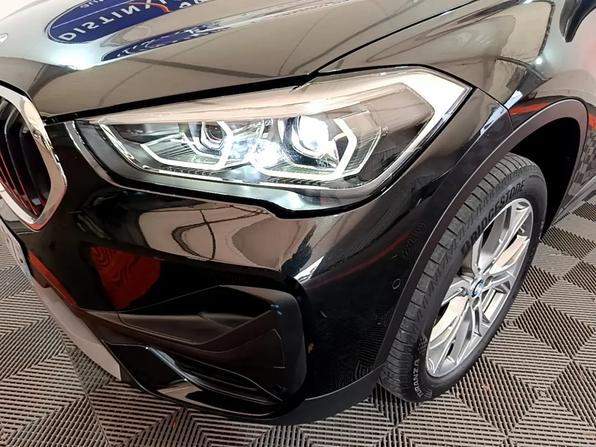 Gros plan sur l'avant droit noir brillant du BMW X1 sDrive16d 2021, mettant en valeur le phare LED et la roue.