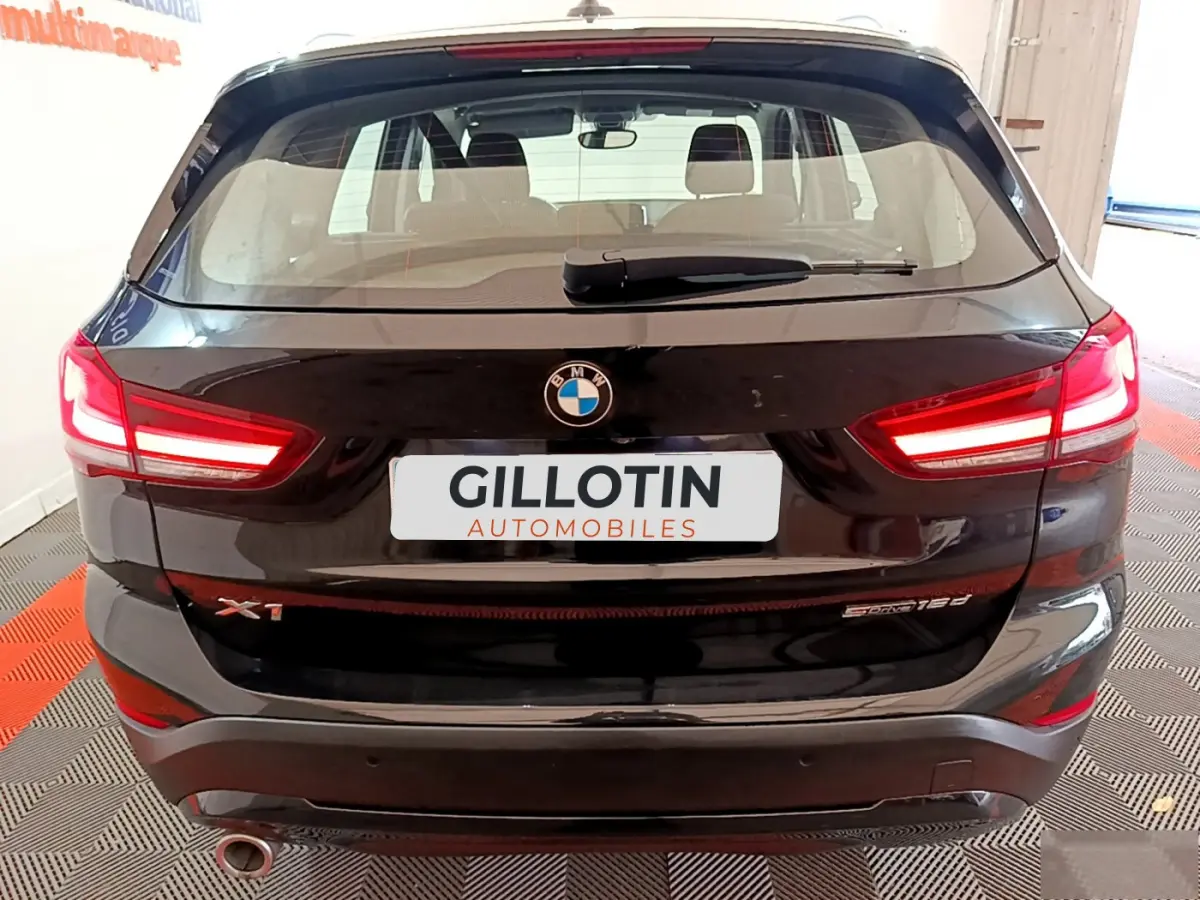 Vue arrière d’un BMW X1 sDrive16d noir avec feux LED allumés et logo visible sur un sol à damier rouge et gris.