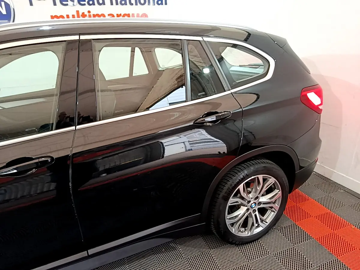 Vue latérale droite d'un BMW X1 noir 2021 avec jante alliage et feu arrière allumé dans un garage.