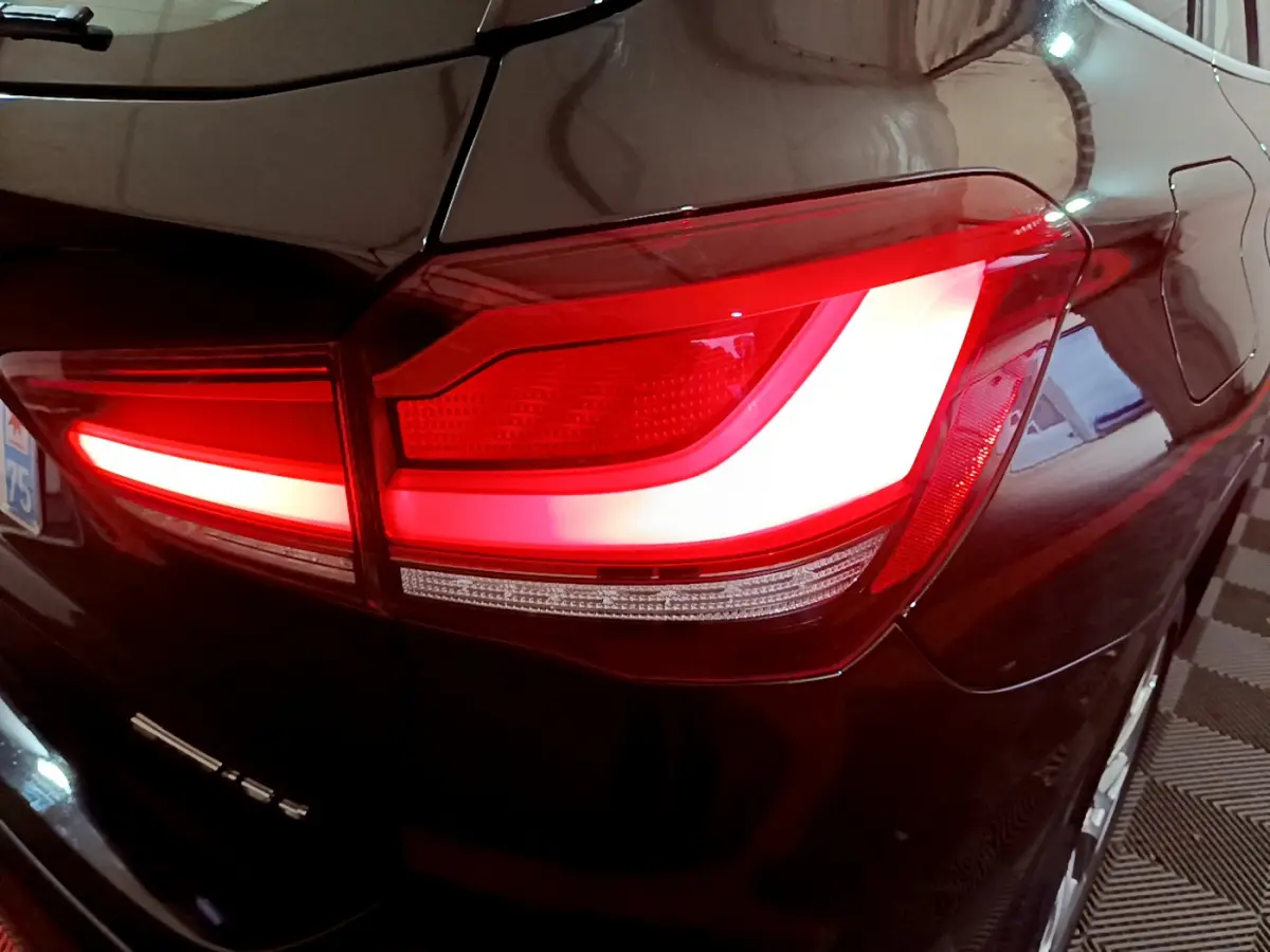 Gros plan sur le feu arrière droit rouge et blanc d’un BMW X1 noir, avec reflet sur la carrosserie brillante.