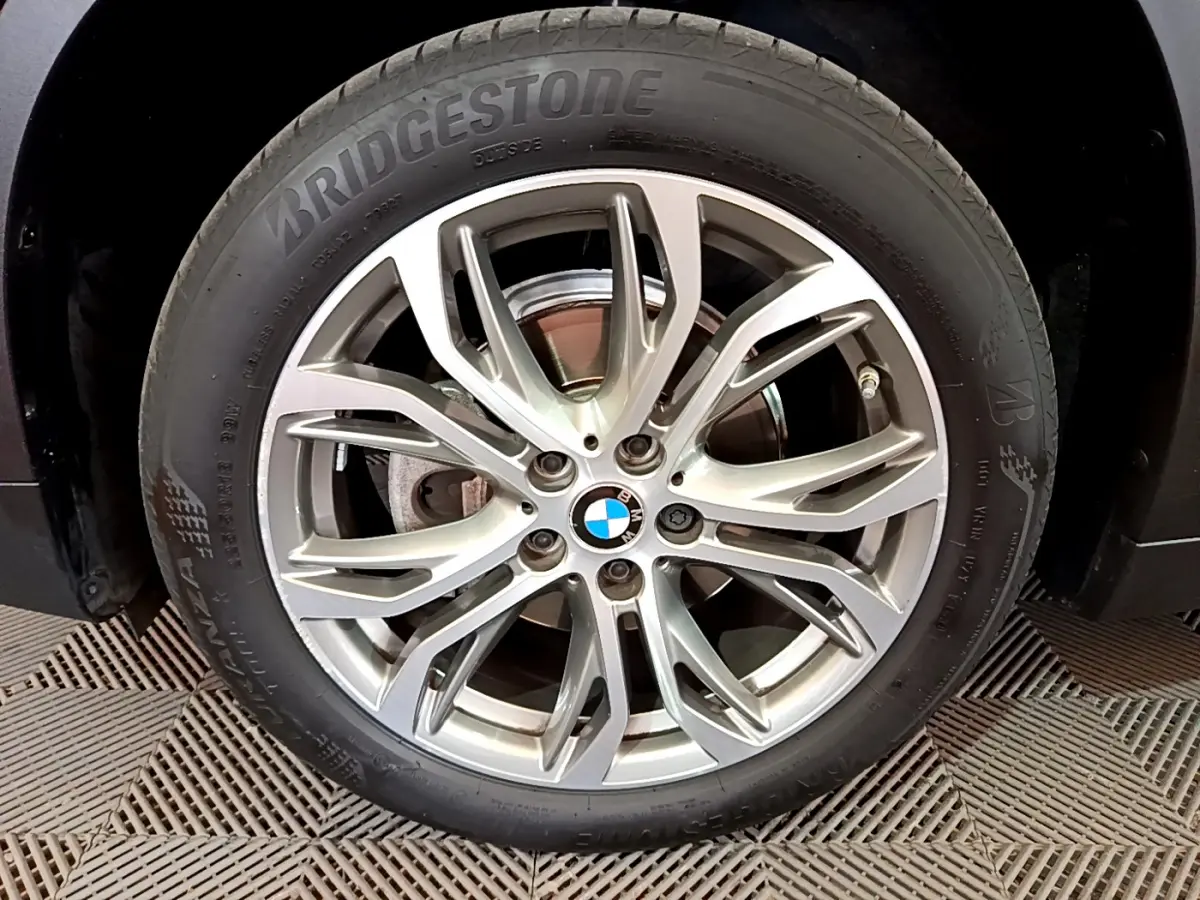 Gros plan sur la roue avant droite d’un BMW X1 noir, jante alliage argentée à design multiple branches.