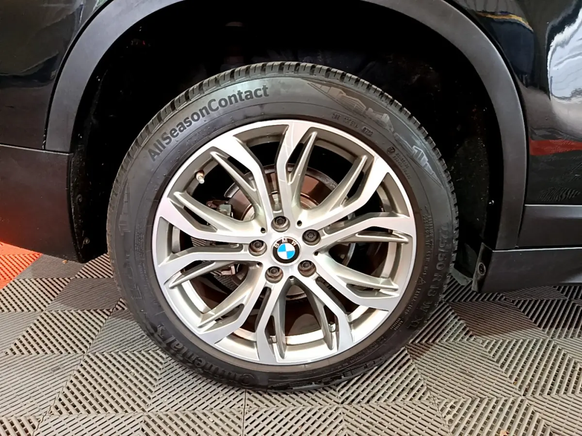 Gros plan sur la roue avant gauche avec jante alliage argentée et logo BMW sur BMW X1 noir sDrive16d Lounge DKG7.