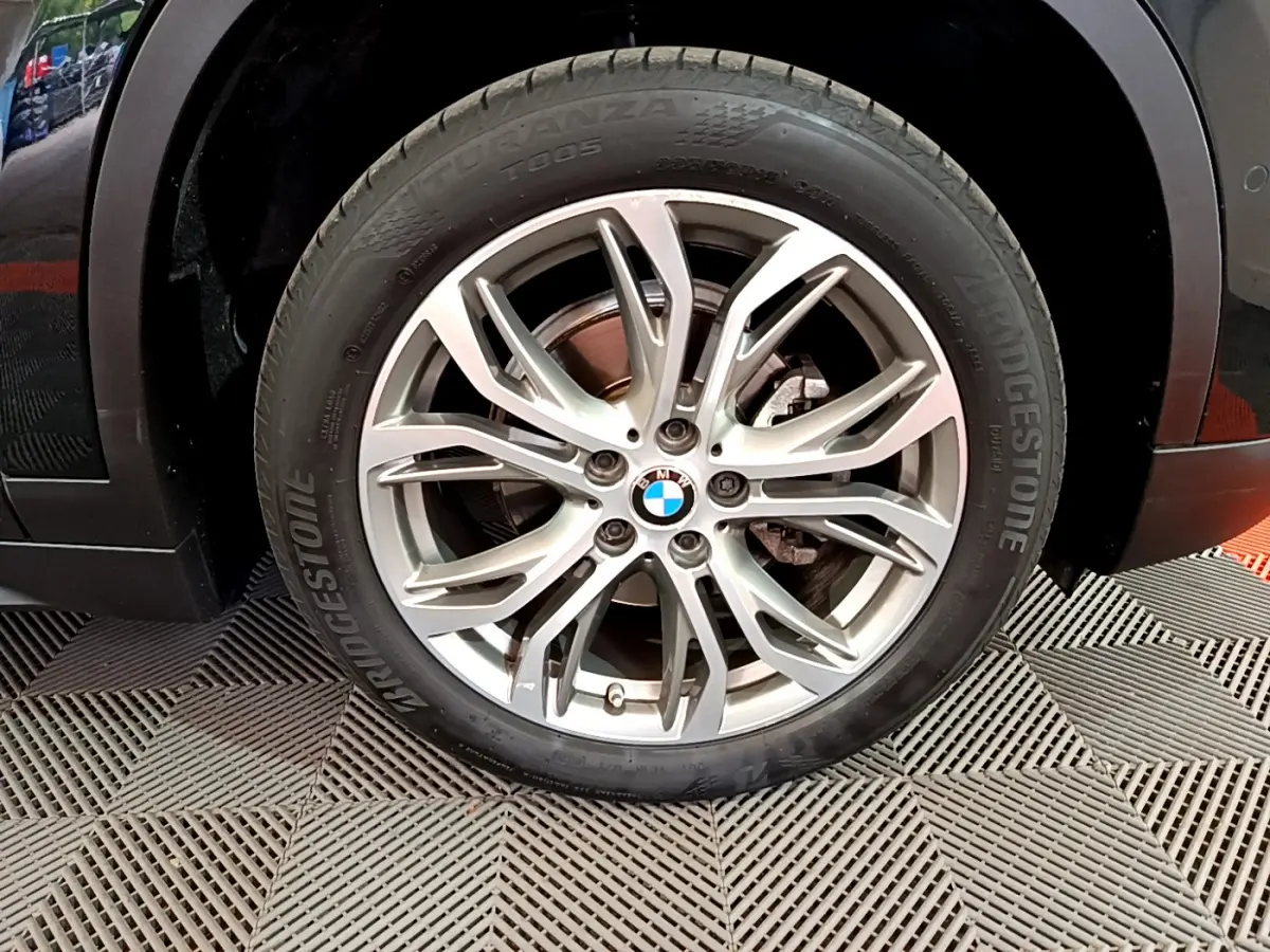Gros plan sur la roue avant droite noire d’un BMW X1 2021 avec jante alliage multi-branches argentée.