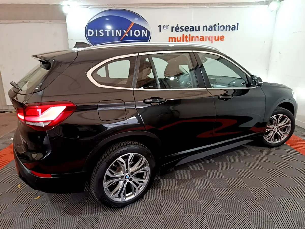 BMW X1 sDrive16d noire vue de profil droit, avec feux arrière allumés dans un showroom intérieur.