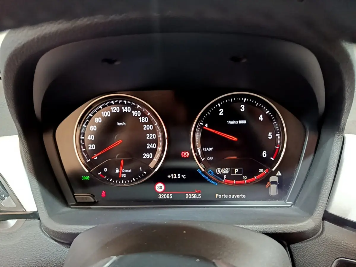 Vue rapprochée du tableau de bord numérique du BMW X1 noir, affichant la vitesse, le régime moteur et les alertes.