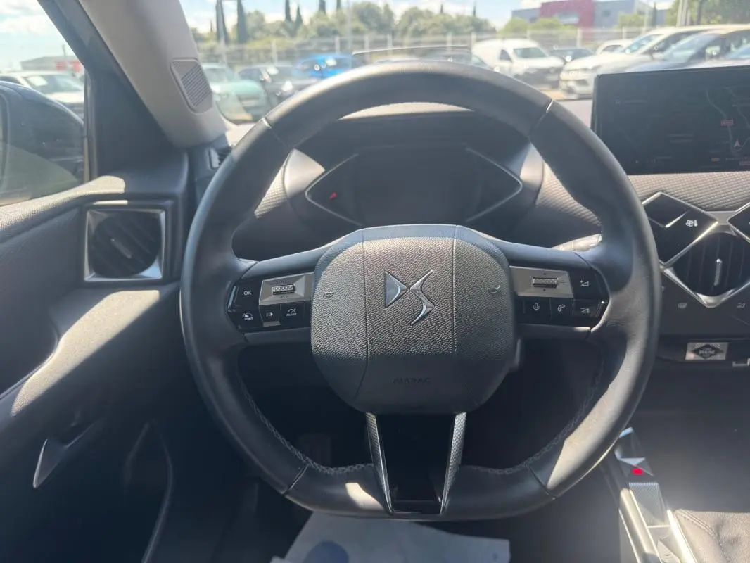 Vue centrée sur le volant noir du DS3 100 BVM6 Bastille 2024 avec tableau de bord et écran tactile en arrière-plan.