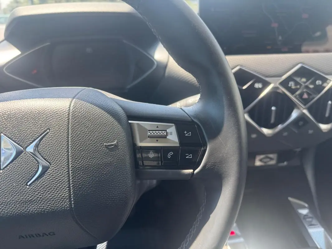 Vue rapprochée du volant noir et de la console centrale avec commandes en losange du DS3 100 BVM6 Bastille gris 2024.