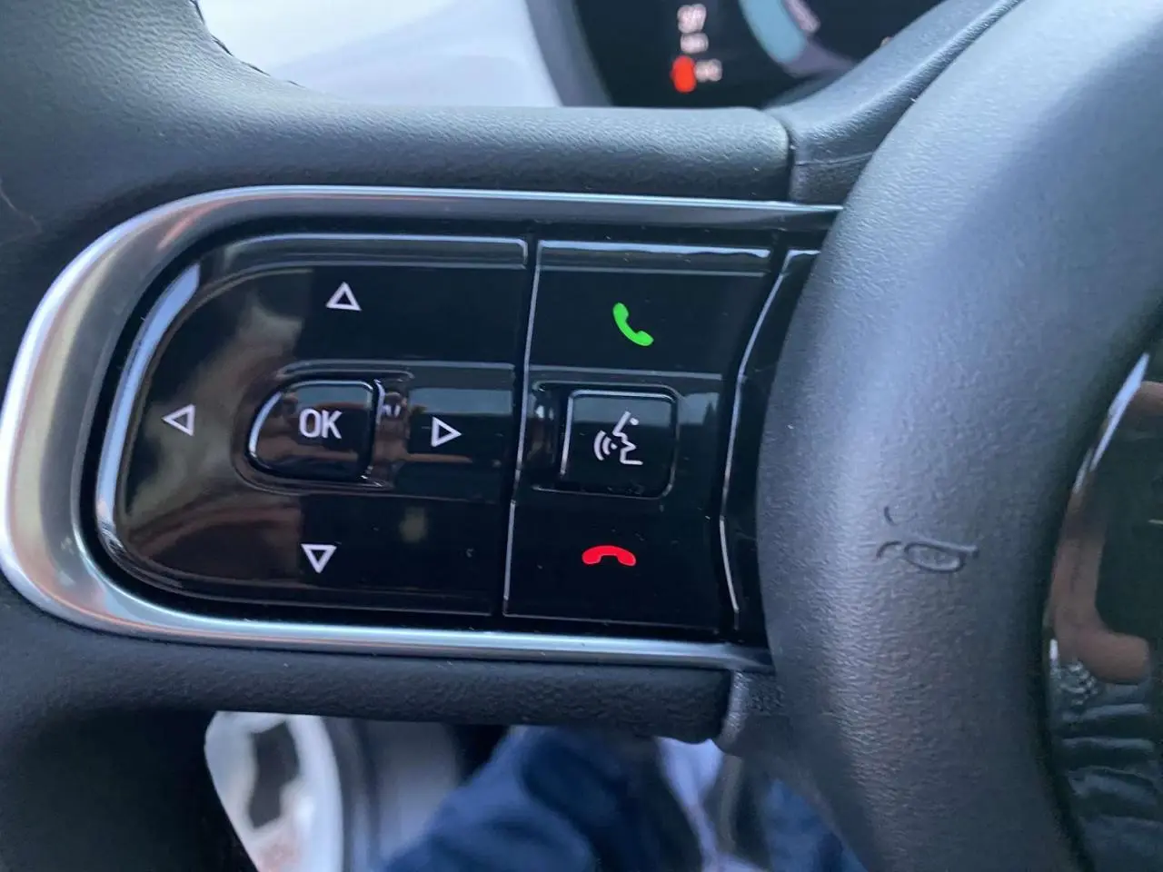 Gros plan sur les commandes noires du volant du Fiat 500 électrique blanc, avec boutons appel et navigation intégrés.