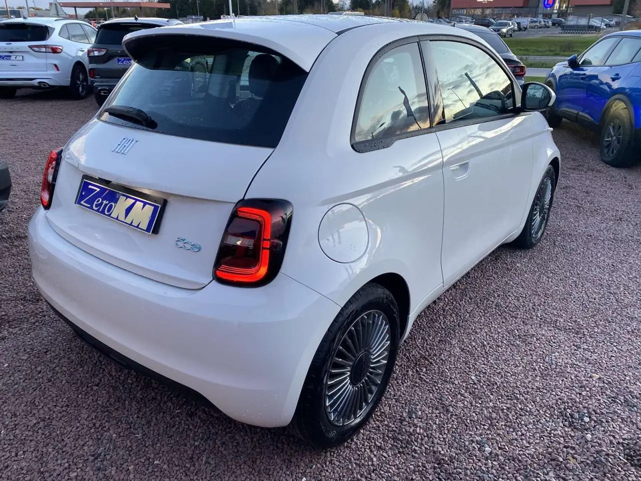 Vue 3/4 arrière droite d'une FIAT 500 électrique blanche avec jantes alliage 16'' Icône sur parking.