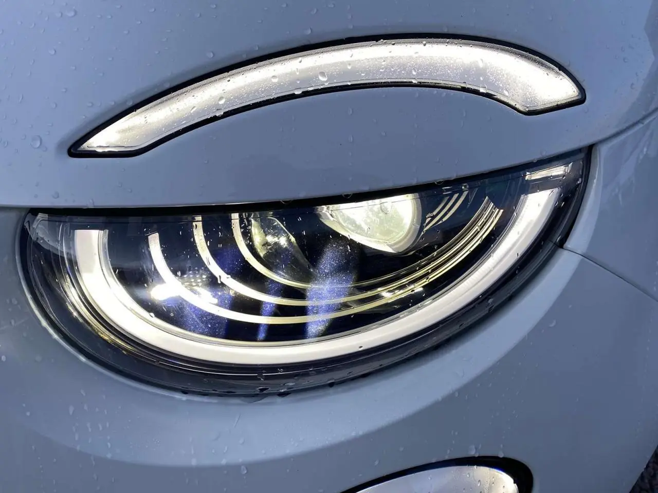 Gros plan sur le phare avant droit blanc d'une FIAT 500 électrique 118CV Icône avec gouttes d'eau visibles.