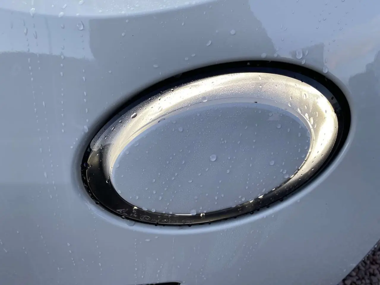 Gros plan sur le feu avant oval blanc d'une Fiat 500 électrique 2022 avec gouttes d'eau sur la carrosserie.
