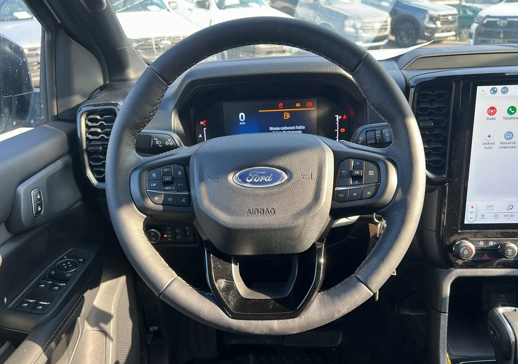 Vue intérieure centrée sur le volant noir du Ford Ranger 2025 blanc glacier, avec tableau de bord digital et écran tactile visible.