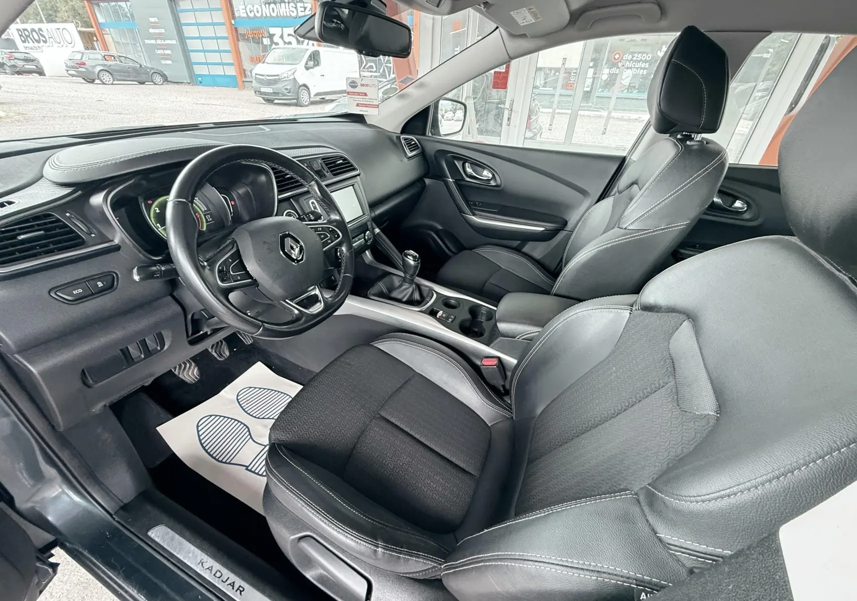 Vue intérieure côté conducteur du Renault Kadjar gris 2016, montrant les sièges en tissu et cuir ainsi que le tableau de bord.