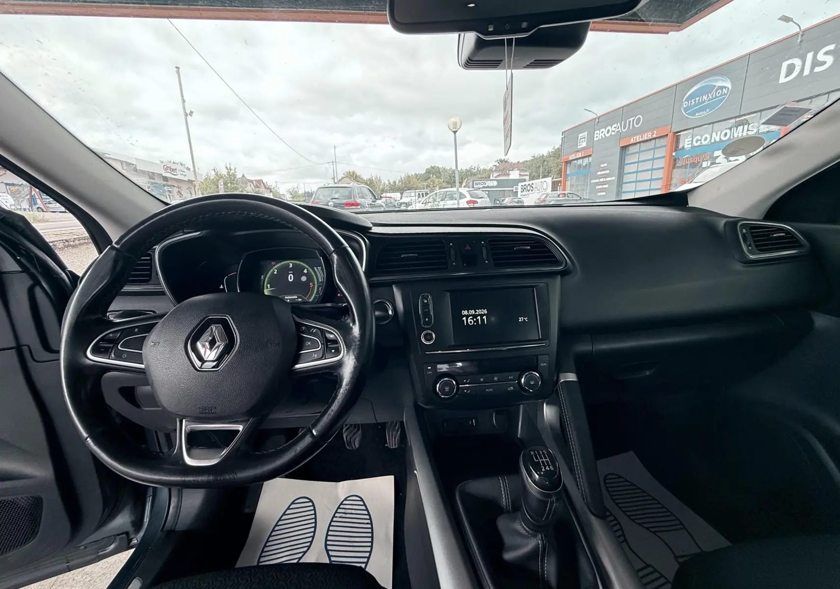 Vue intérieure avant du Renault Kadjar gris, montrant le volant, tableau de bord et levier de vitesses manuel.