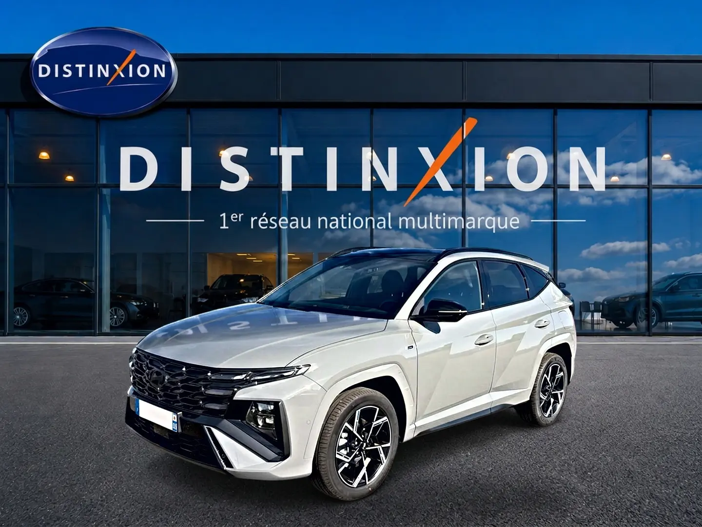 Hyundai Tucson 2026 gris shadow en 3/4 avant droit devant showroom Distinxion, jantes alu noires et toit noir.