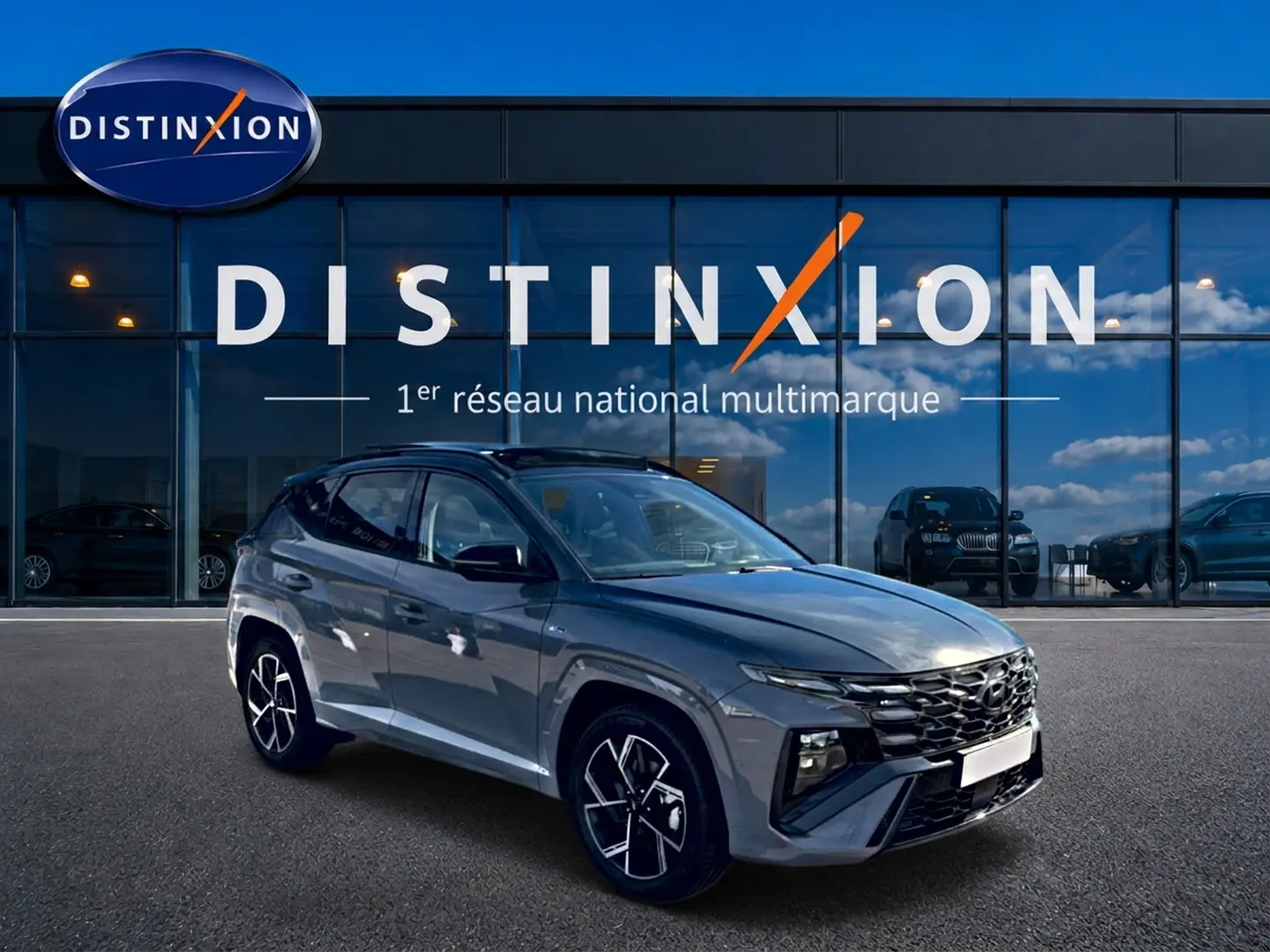 Hyundai Tucson gris shadow en 3/4 avant droit, avec calandre noire et jantes alu distinctives devant showroom Distinxion.