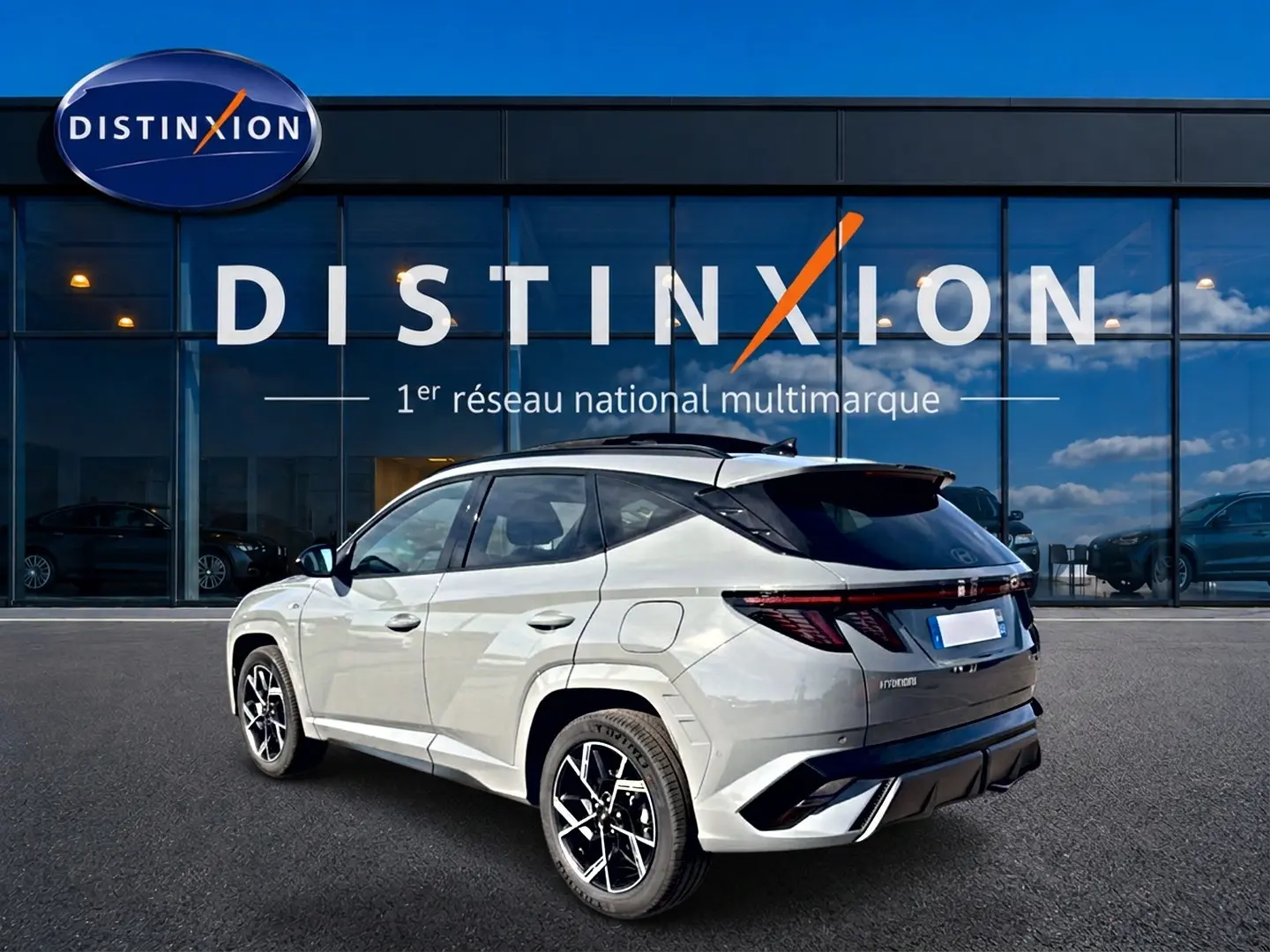 Vue 3/4 arrière droite du Hyundai Tucson gris shadow avec jantes alu et toit noir devant une vitrine Distinxion.