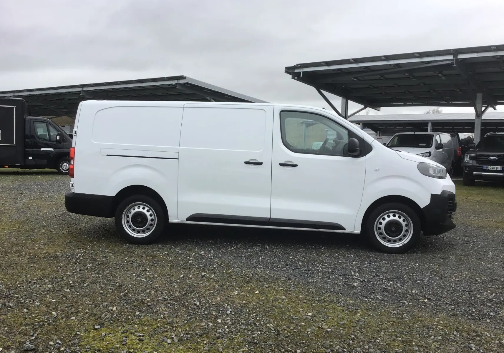 Vue de profil côté droit d’un FIAT Scudo Fourgon blanc 2024 avec porte latérale coulissante, stationné sur sol gravillonné.