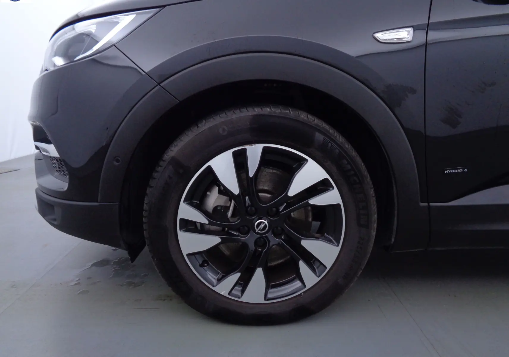 Gros plan sur la roue avant gauche noire métallisée d'un Opel Grandland X hybride avec jante alliage bicolore.